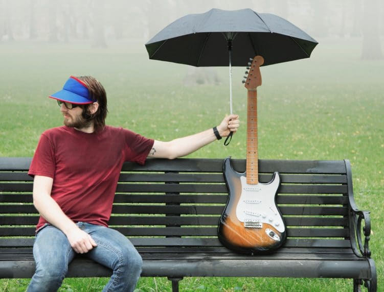 Mann auf Bank mit Schirm über Gitarre Quatsch als Einfall im Redaktionsplan